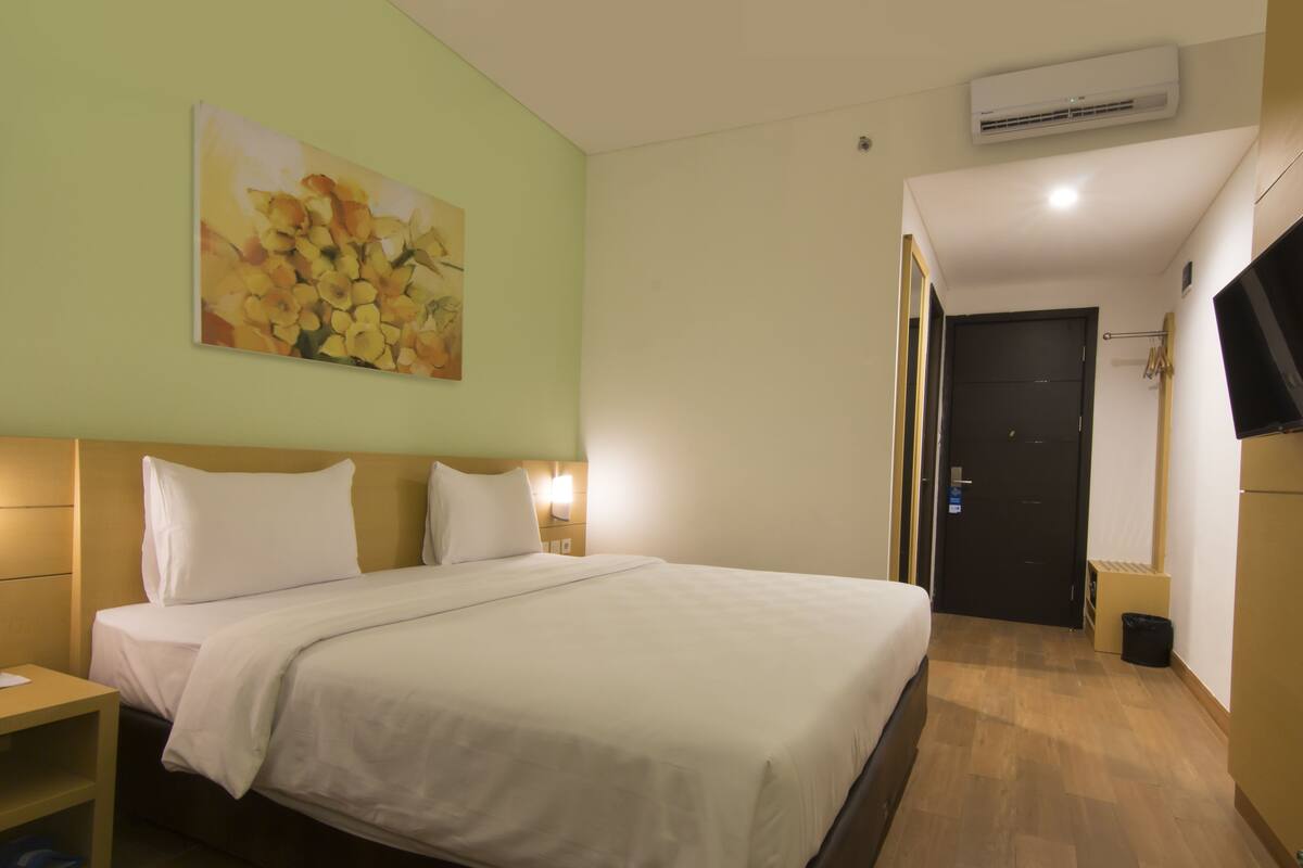 Une chambre d’hôtel avec un lit, une table de chevet, un climatiseur fixé au mur et un tableau.
