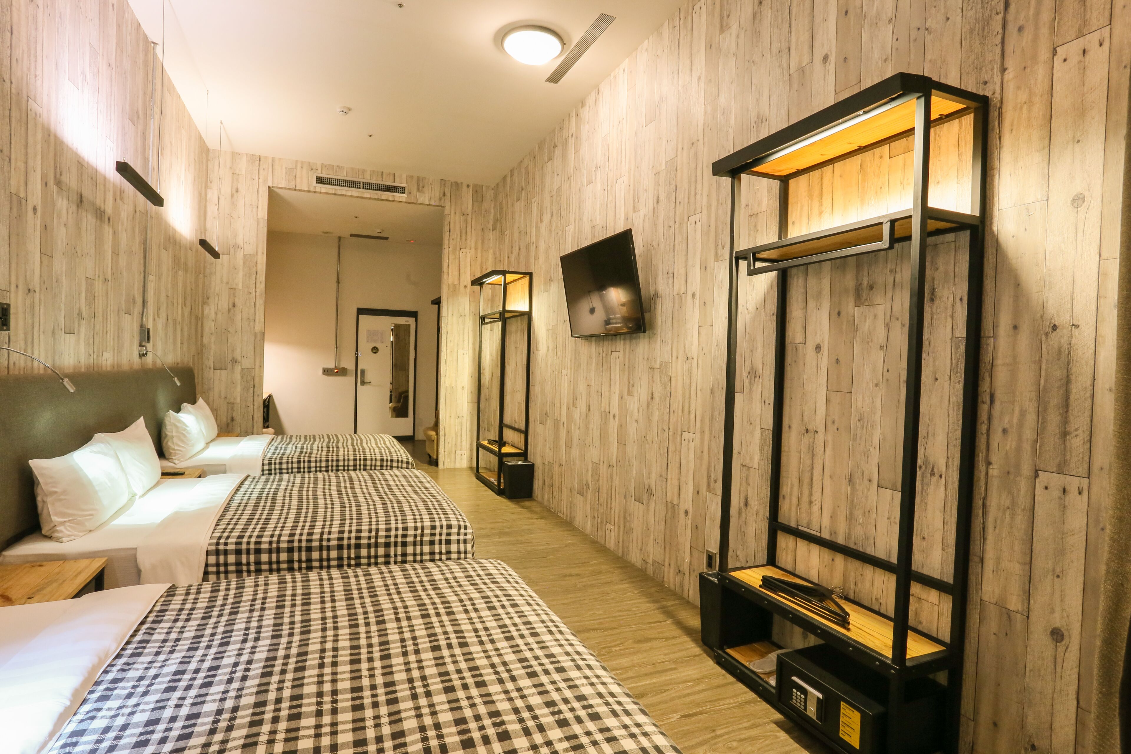 A hotel room with a checkered bedspread, a flat-screen TV mounted on the wall, and a wooden floor.