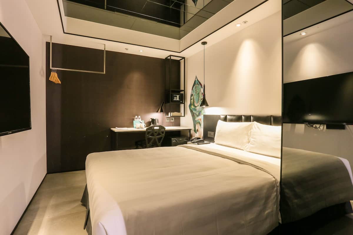 A modern hotel room with a large bed, a desk with a chair, a flat-screen TV, and a large mirror.