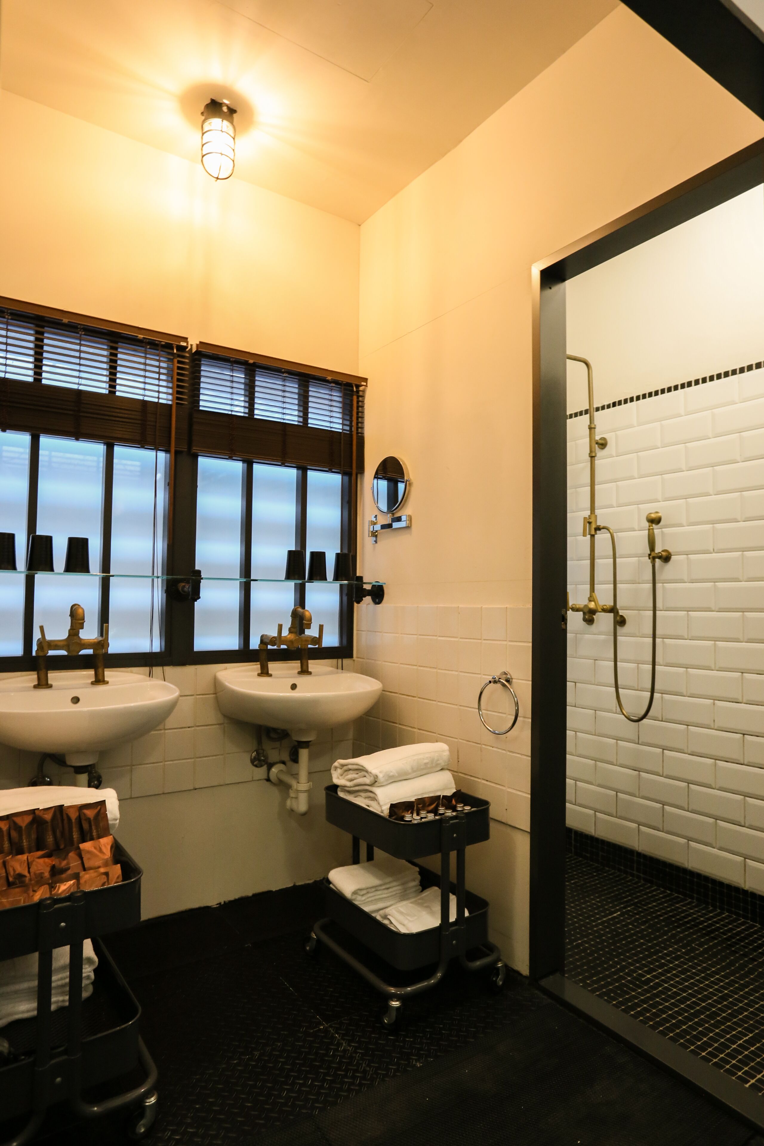A bathroom with two sinks, a shower, and a window with blinds.
