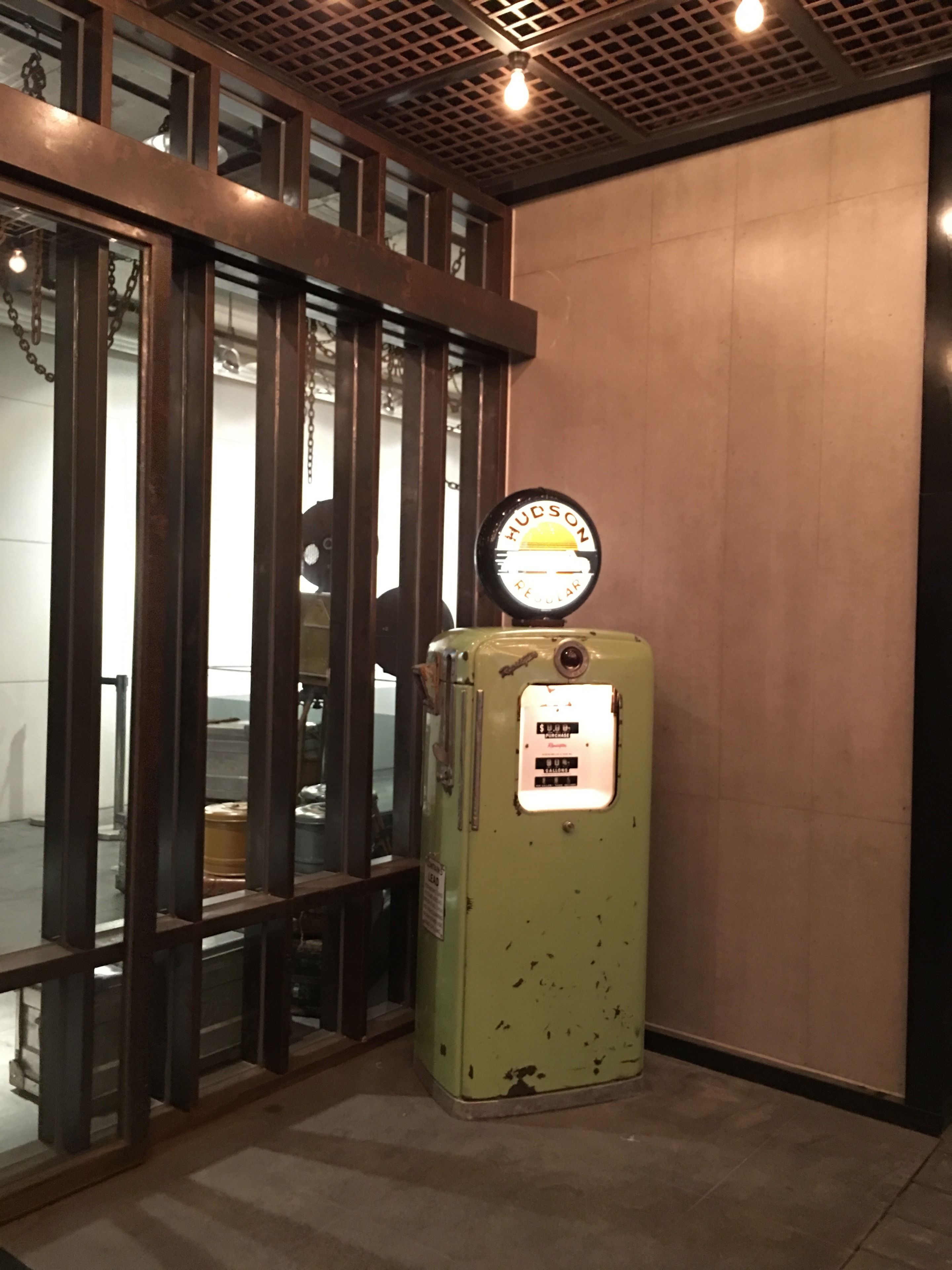 A vintage Hudson refrigerator with a sign, placed against a wall with a metal grid ceiling and wooden beams.