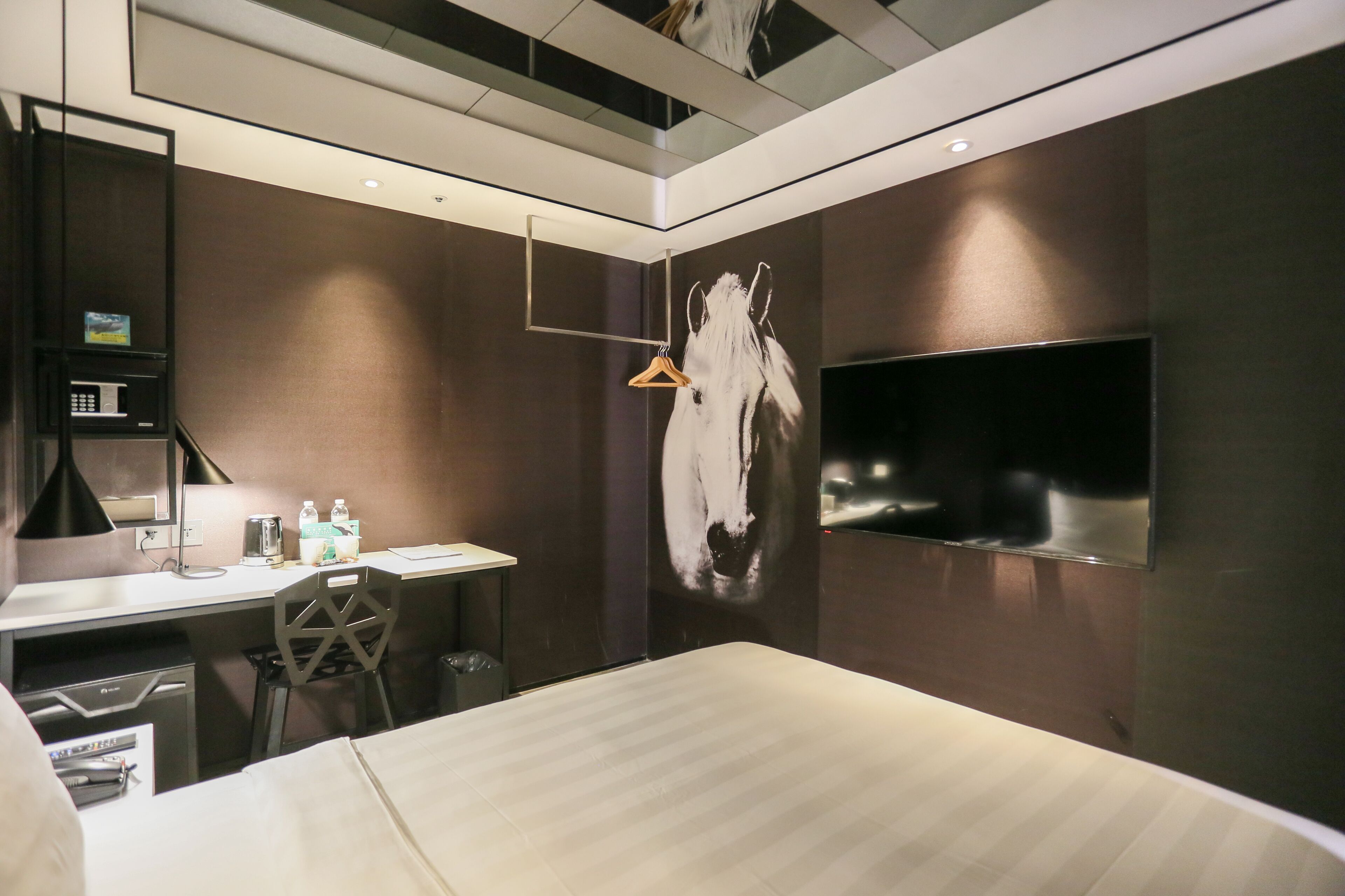 Una habitación de hotel moderna con una cama grande, un escritorio con silla, un televisor montado en la pared y una lámpara colgante.