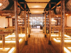 A wooden floor with tables and chairs under a thatched roof structure.