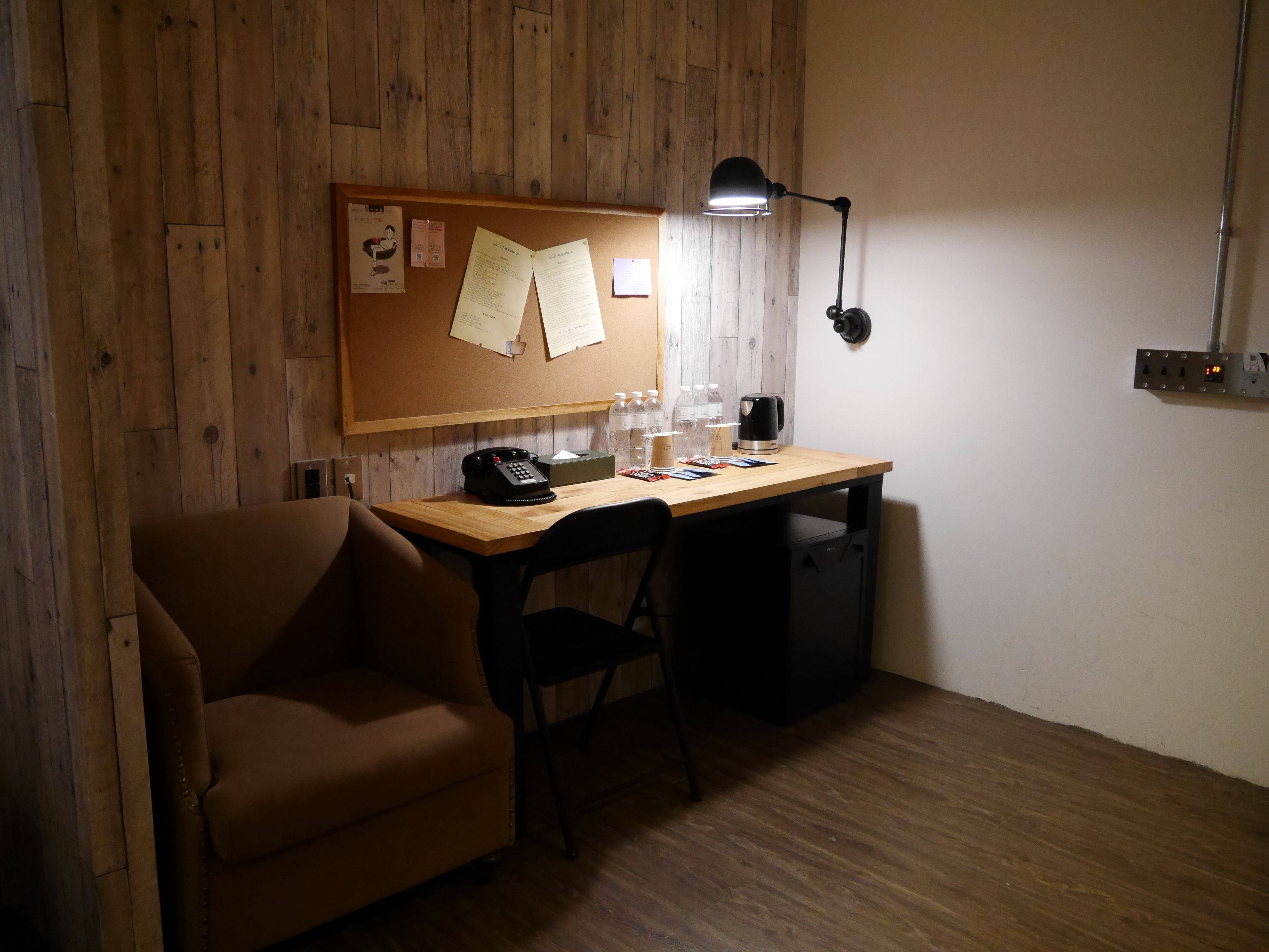 A small office space with a wooden desk, a chair, a desk lamp, a telephone, and a bulletin board with papers.
