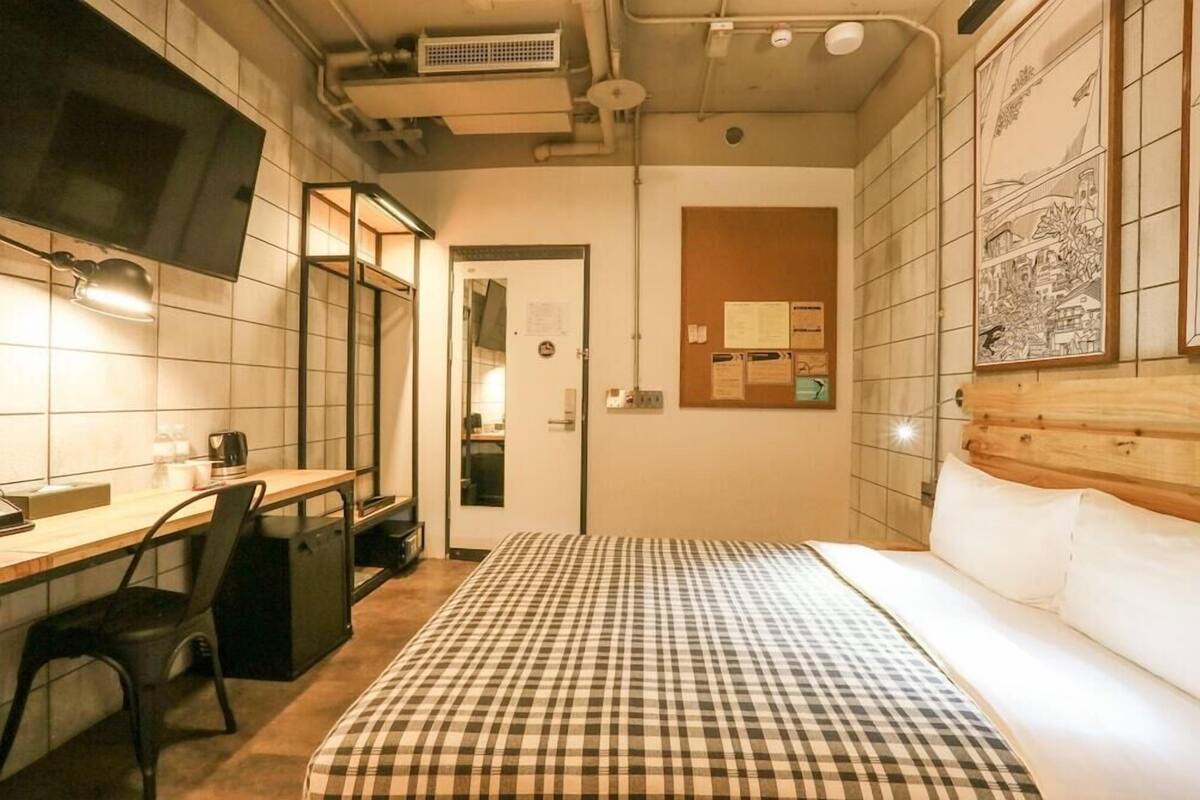 A compact hotel room with a bed, a desk, a chair, and a television mounted on the wall.