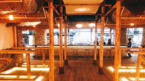 An indoor dining area with wooden tables and chairs, stone walls, and a thatched roof. - Hotel Papa Whale (Taipei)