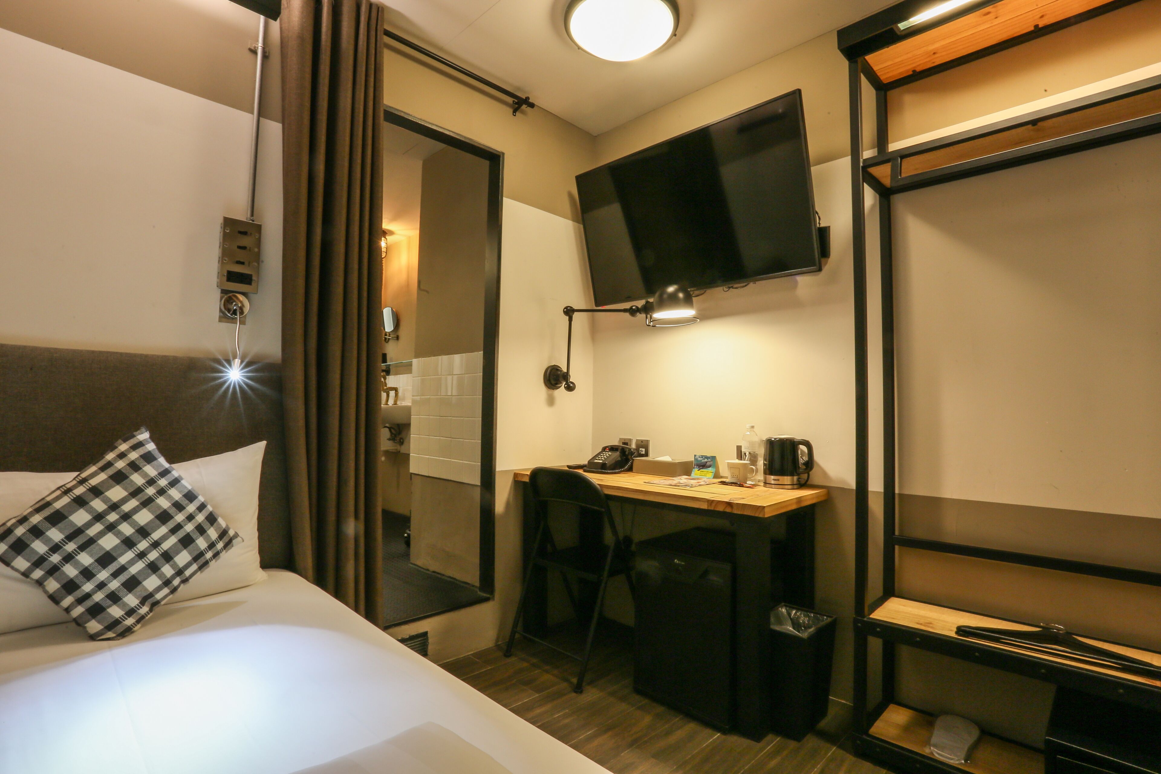 A hotel room with a bed, a desk, a chair, a television, and a small shelf.
