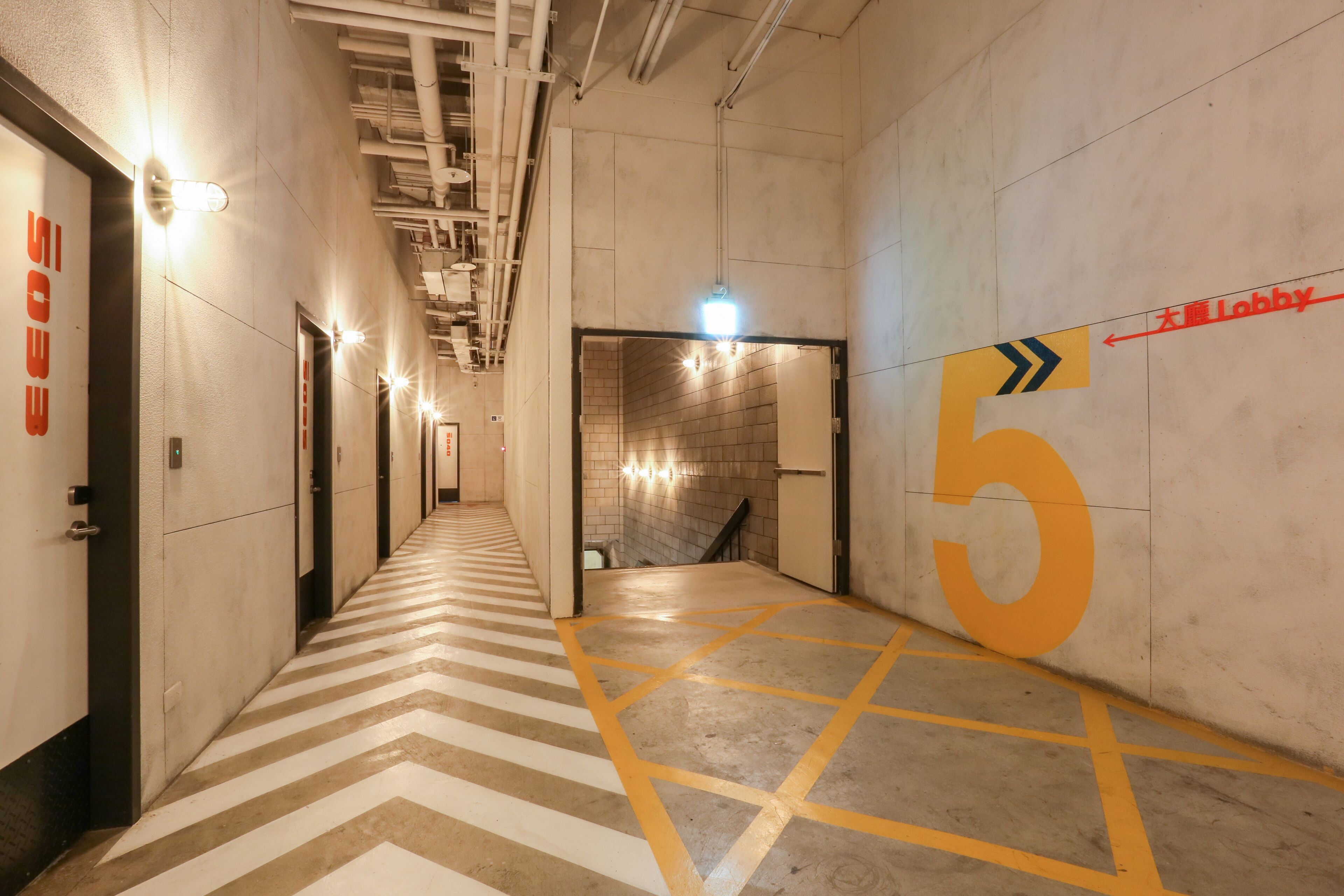 Un couloir avec un sol à motifs en chevron, un grand chiffre « 5 » peint sur le mur et des flèches indiquant la direction du hall d’entrée.
