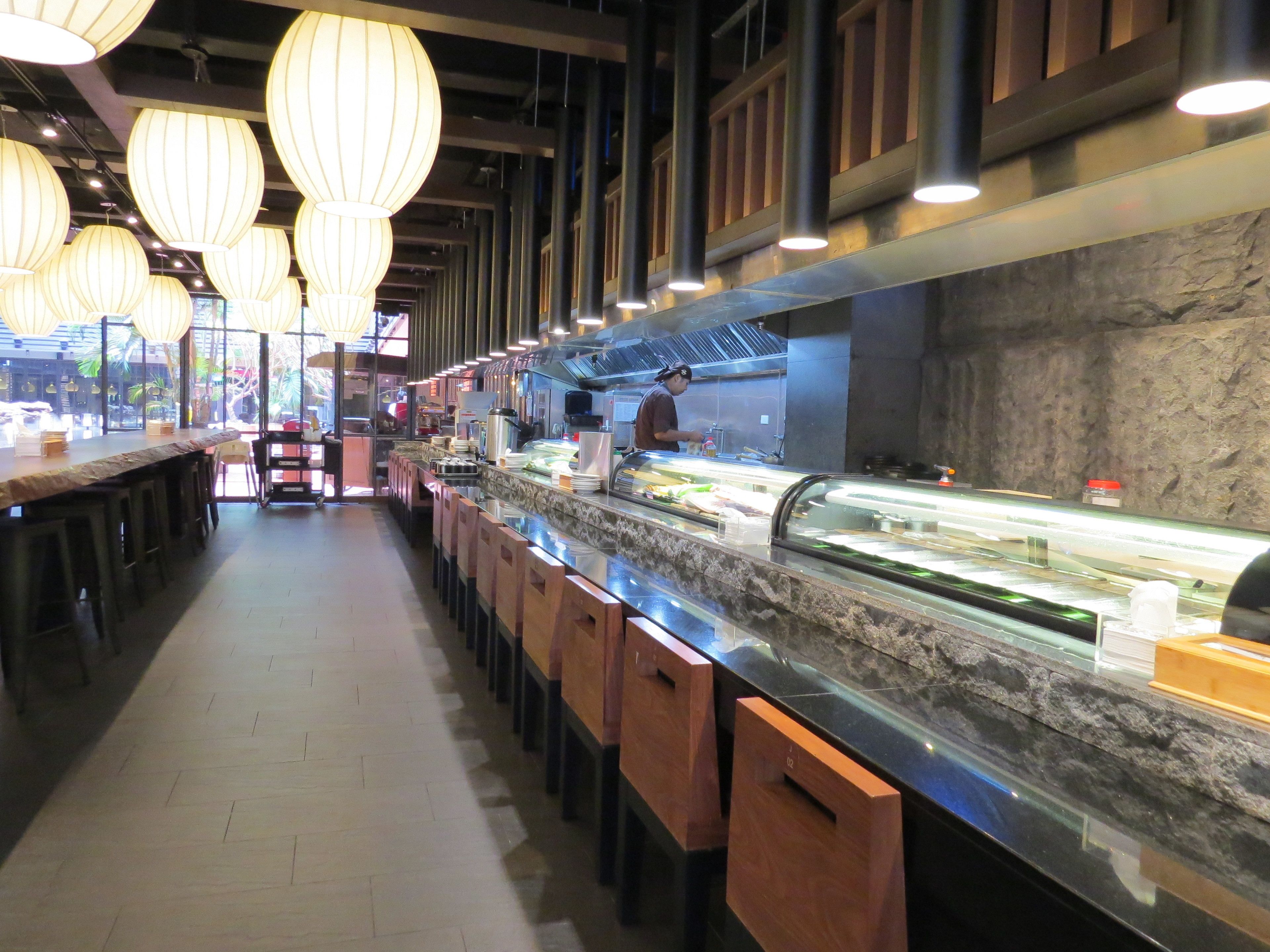 A restaurant with a long counter, bar stools, and hanging paper lanterns.