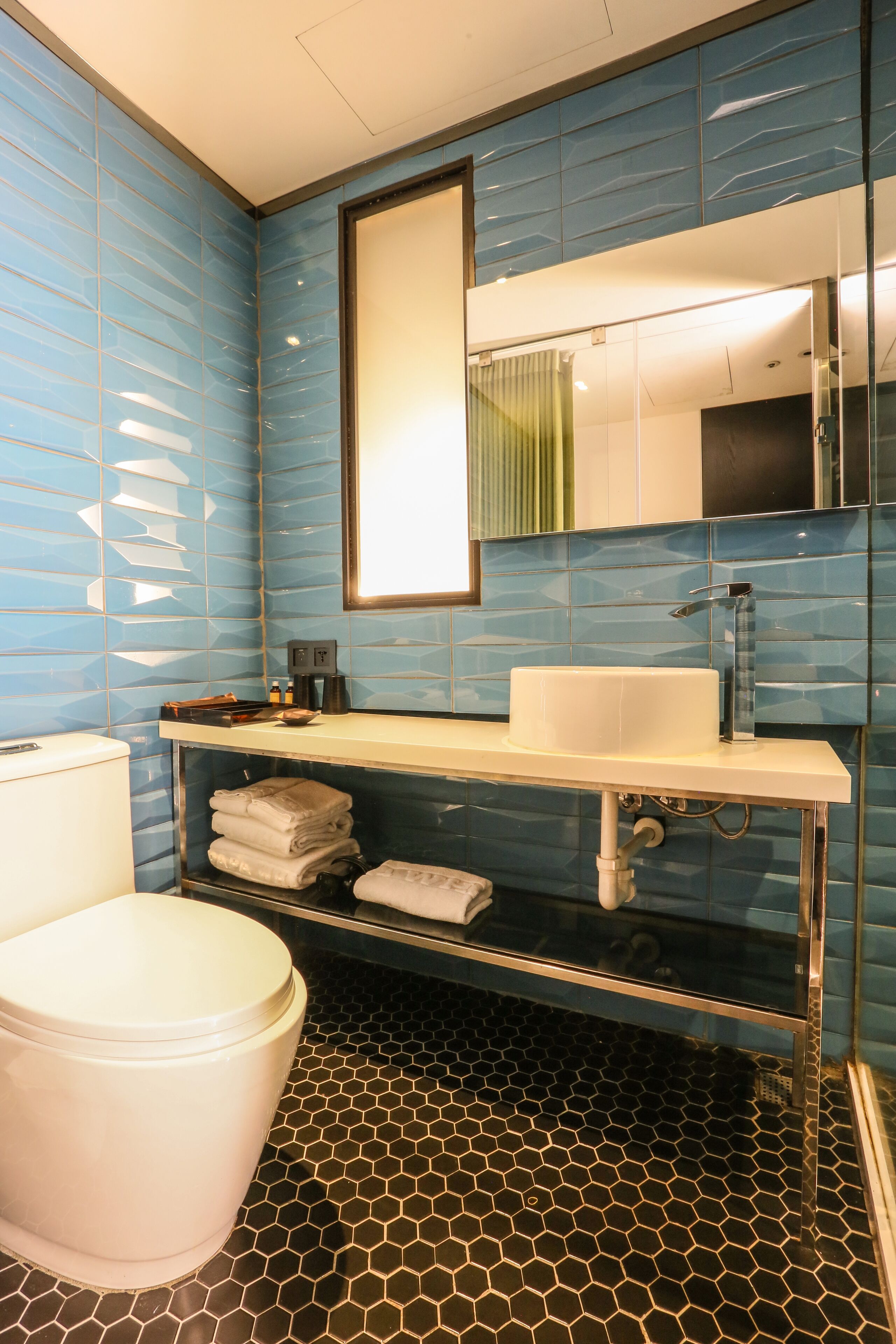 Un baño con inodoro blanco, un lavabo con espejo y suelo de baldosas.