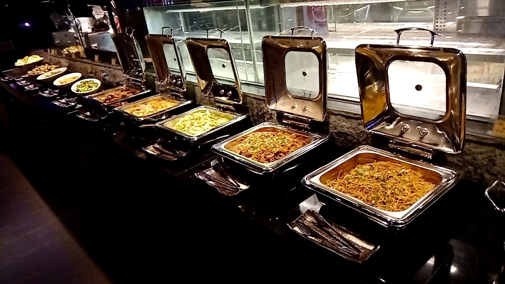 A buffet line with various dishes in metal serving trays.