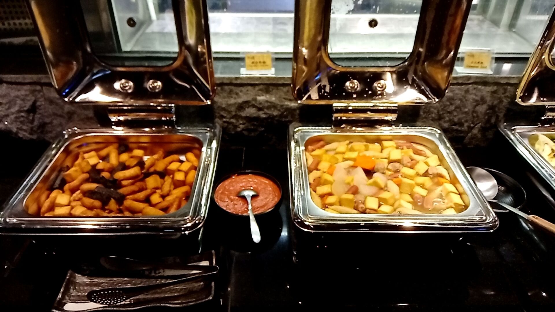 A buffet with various food items in metal containers, including fries and cubed vegetables.