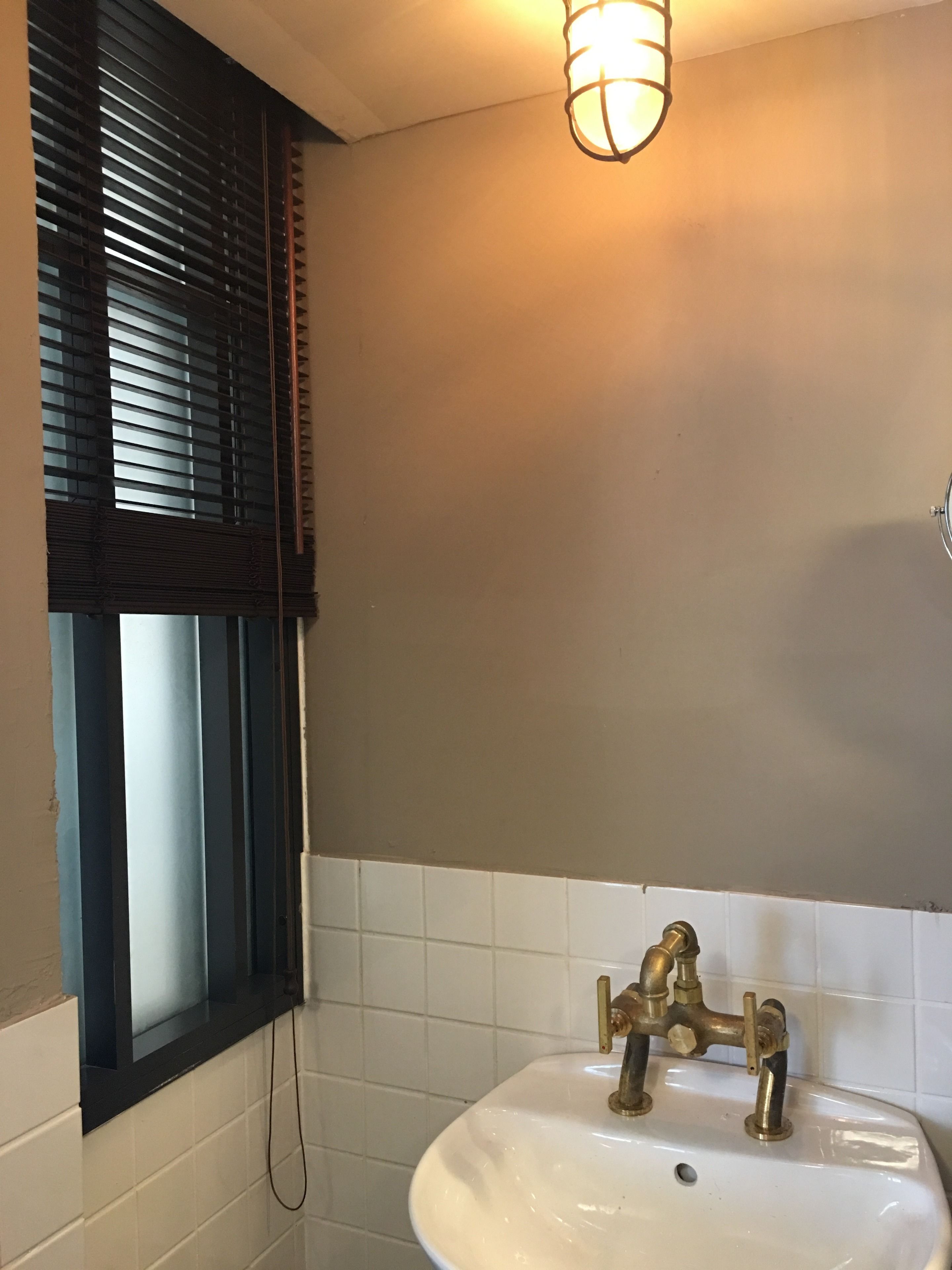 Een badkamer met een wit wastafel, messing kranen en een raam met donkere jaloezieën.