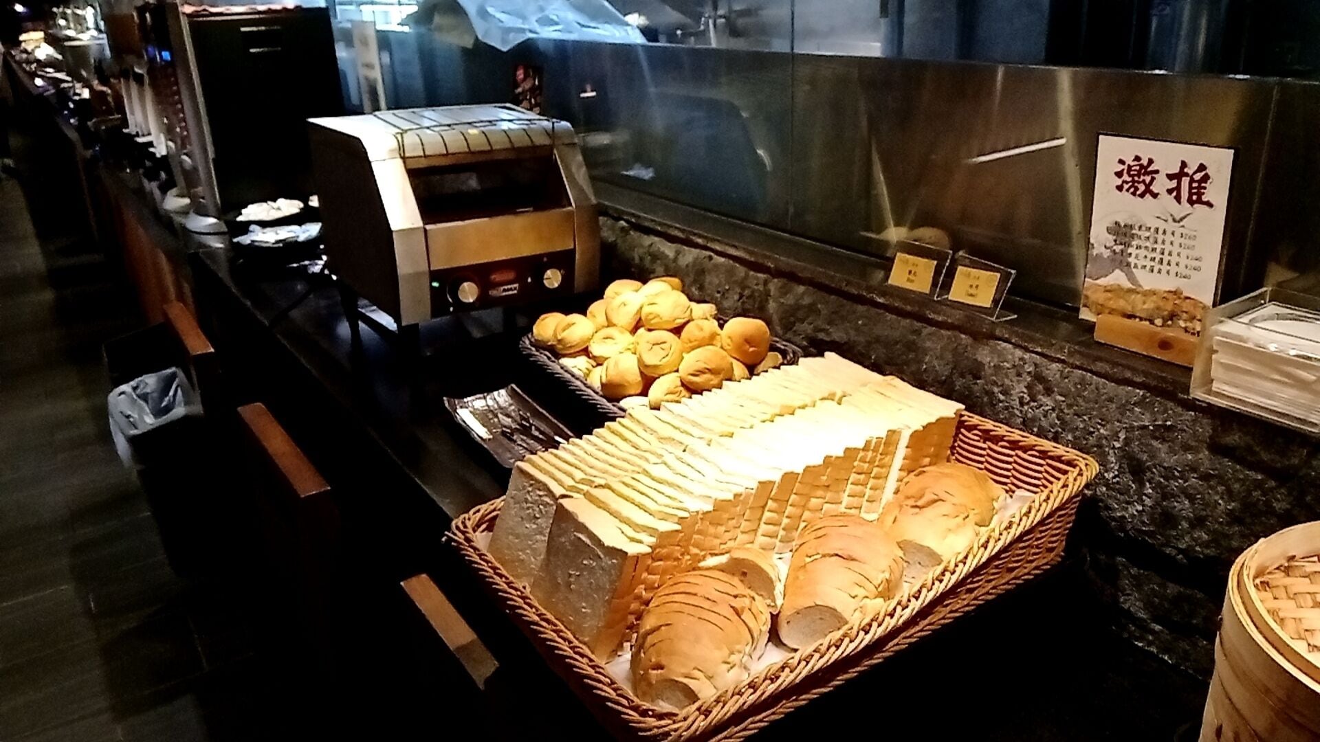 Un espace buffet proposant divers plats, notamment du pain et des petits pains, ainsi qu’un panneau avec des caractères chinois.