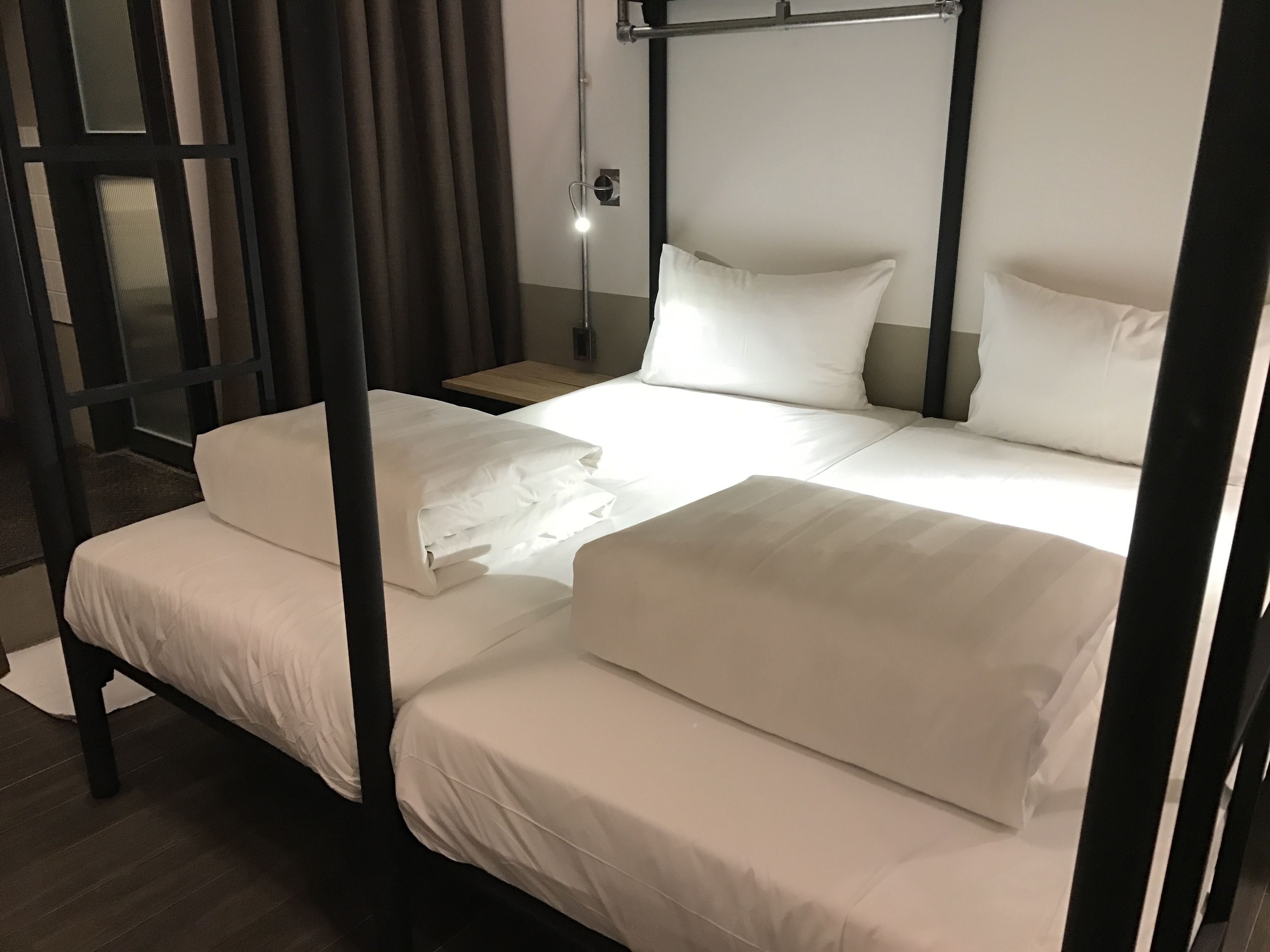 A four-poster bed with white linens, a wooden nightstand, and a wall-mounted light fixture.