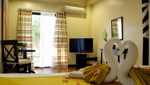 Een hotelkamer met een bed, een televisie, een bureau met stoel, en een raam met gordijnen.