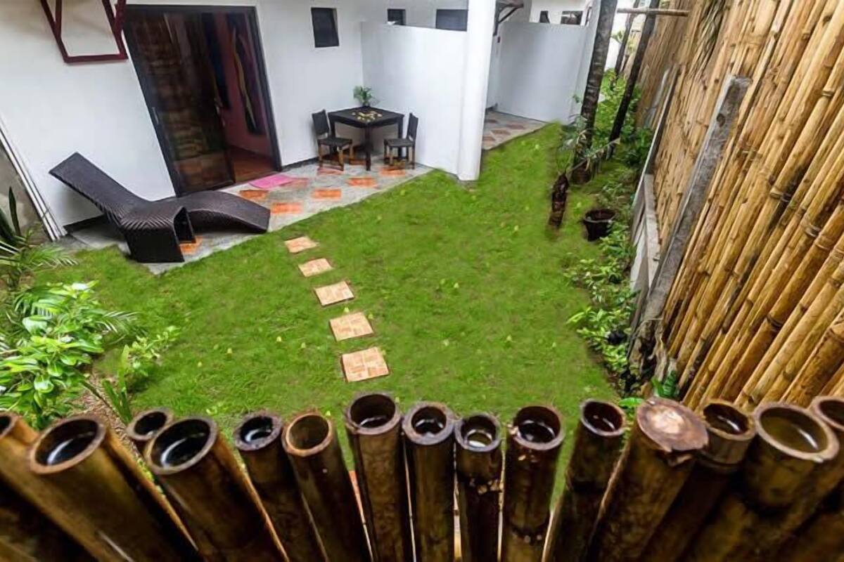 Un jardin avec une pelouse, une petite table et des chaises, et une clôture en bambou.