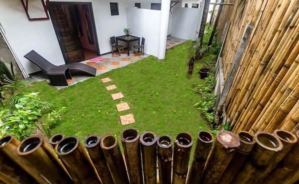 A backyard with a grassy area, a small table with chairs, and a bamboo fence.