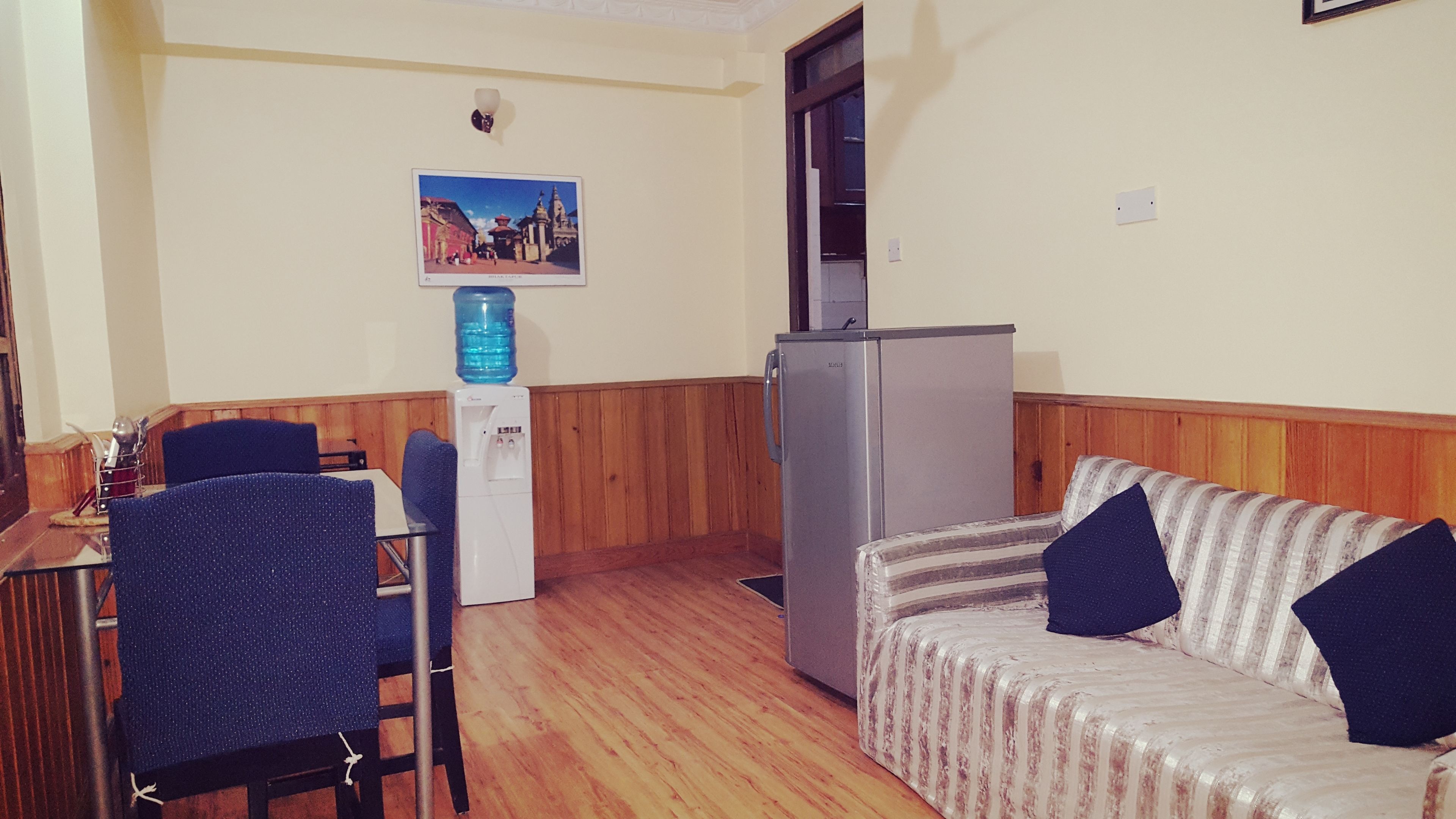 A compact living space with a sofa, chairs, a small table, a refrigerator, and a water dispenser.