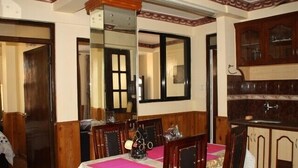 A dining area with a table set for four, wooden chairs, a mirror above the table, and a kitchen area with cabinets and a sink. - Thamel Apartments Hotel (Kathmandu)