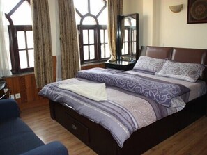 A bedroom with a large bed, a dresser, a mirror, and a window with curtains.