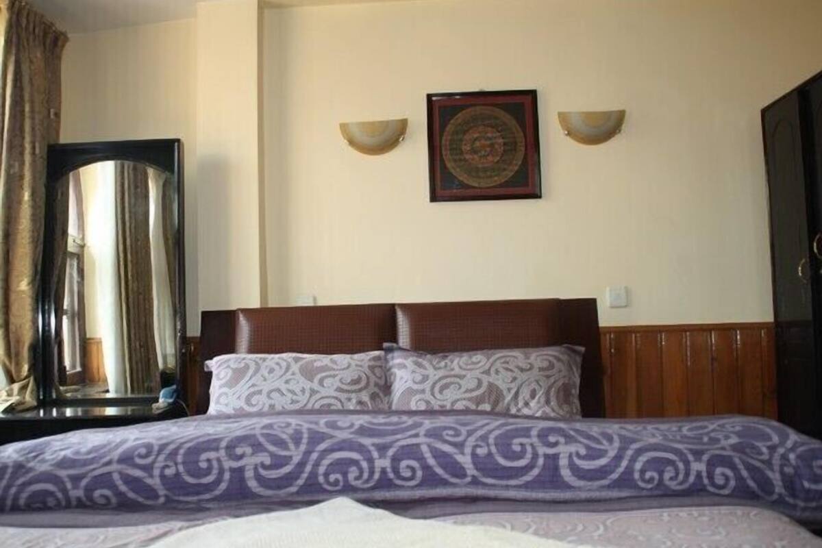 Una camera d'albergo con un letto, tende, un quadro incorniciato e applique.