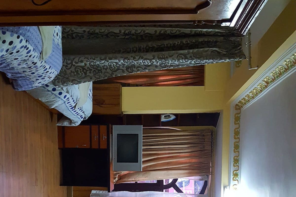 Una stanza con un letto, una televisione, una ventola e tende.