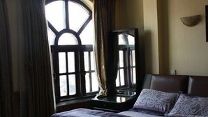 A bedroom with a large bed, a window with curtains, and a wall-mounted light fixture. - Thamel Apartments Hotel (Kathmandu)