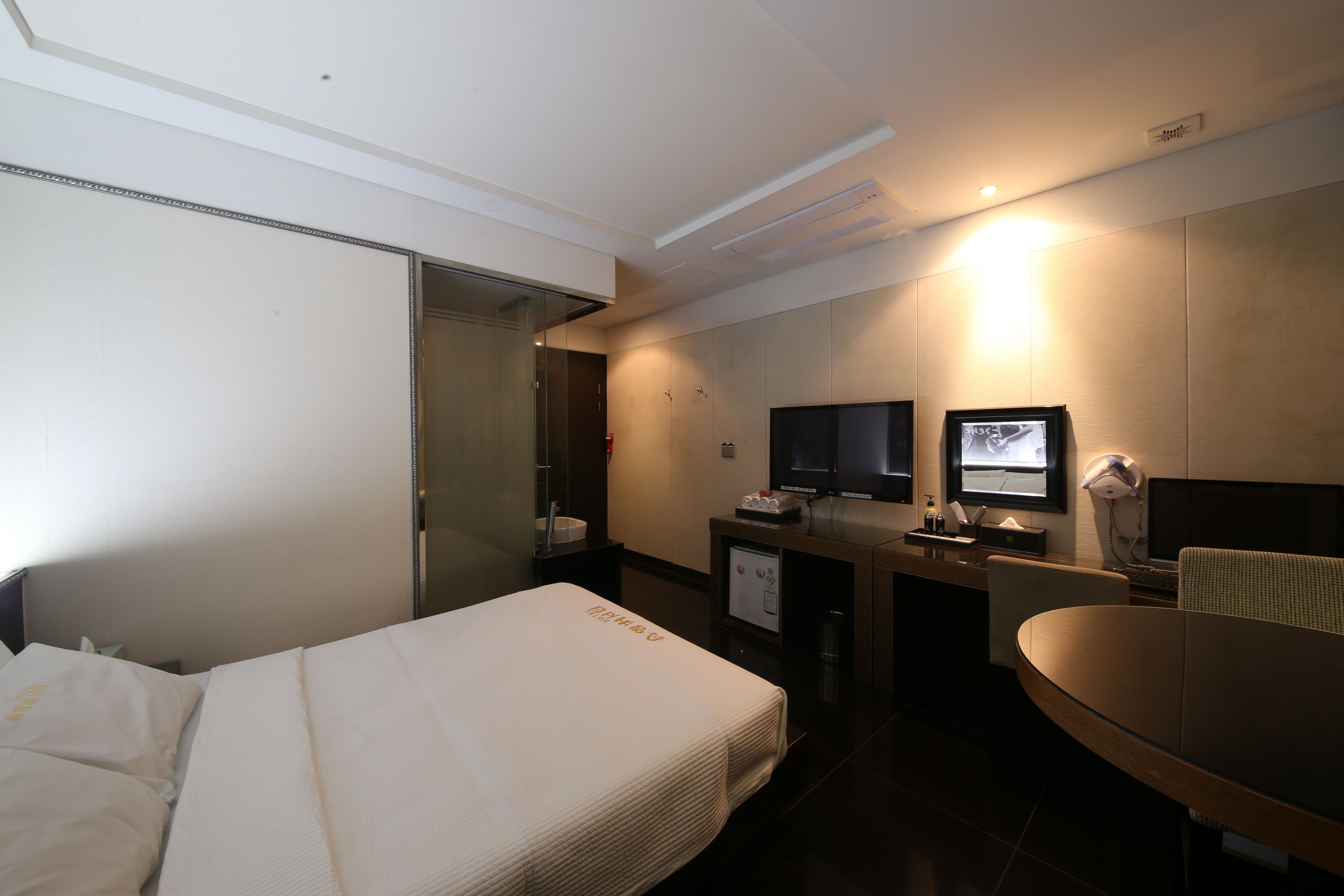 Een moderne hotelkamer met een bed, bureau, stoel, televisie en een kleine kitchenette.
