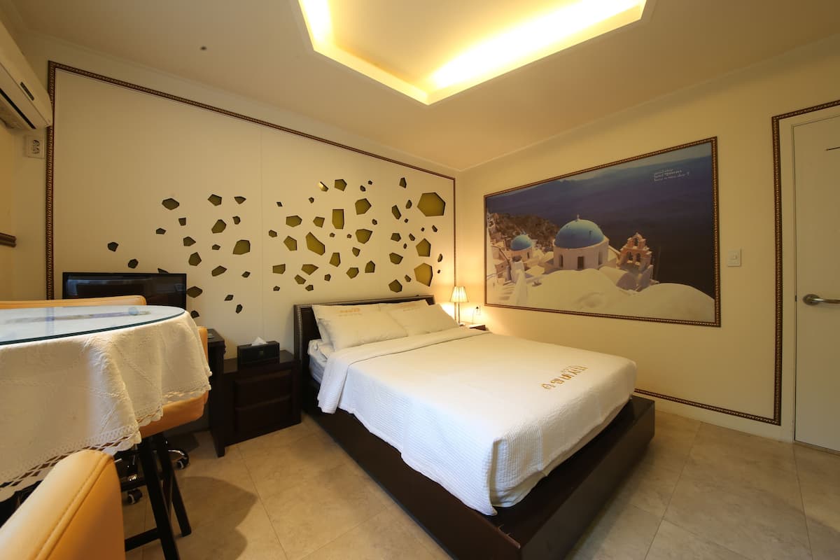 A hotel room with a bed, a desk with a computer, a TV, and a wall with a mosaic design.