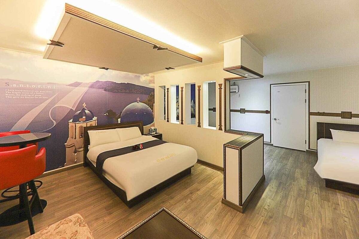 A hotel room with a bed, a desk, a chair, a minibar, and a large window.