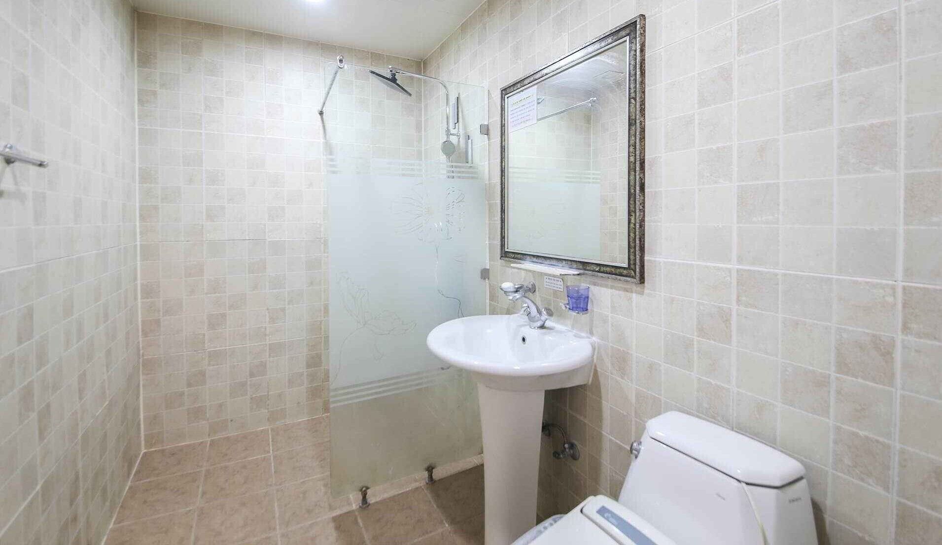 Un baño con ducha de vidrio, lavamanos pedestal y retrete.