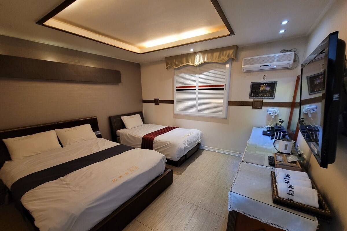 A hotel room with two beds, a desk with a mirror, and an air conditioning unit on the wall.