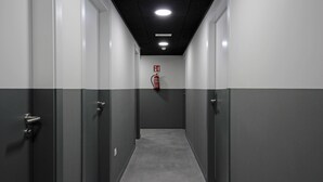 Un pasillo estrecho con paredes grises y blancas, puertas a ambos lados y un extintor montado en la pared.