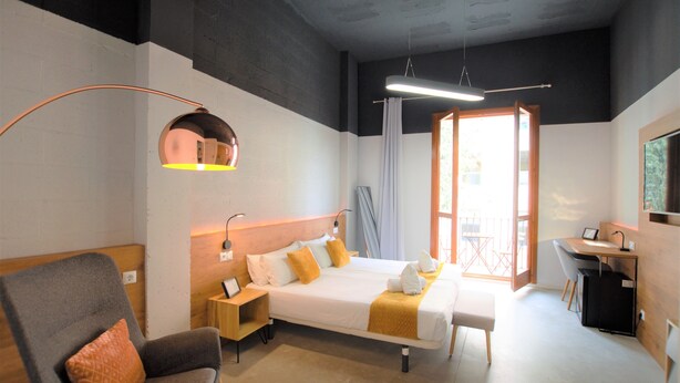 Habitación de hotel con cama, escritorio, silla y un amplio ventanal.