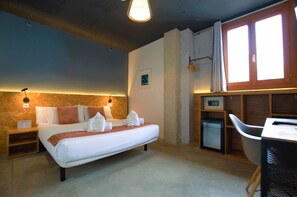 A hotel room with a bed, bedside tables, a desk, a chair, a small fridge, and a window with curtains. - Brick Palma (Palma de Mallorca)