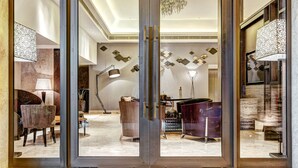 A modern interior with a glass door leading to a well-lit room featuring a chandelier, seating area, and a large table. - THE WAY Dhaka (Dhaka)