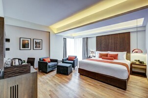 Una habitación de hotel moderna con una cama grande, dos sillones, un escritorio y suelo de madera.