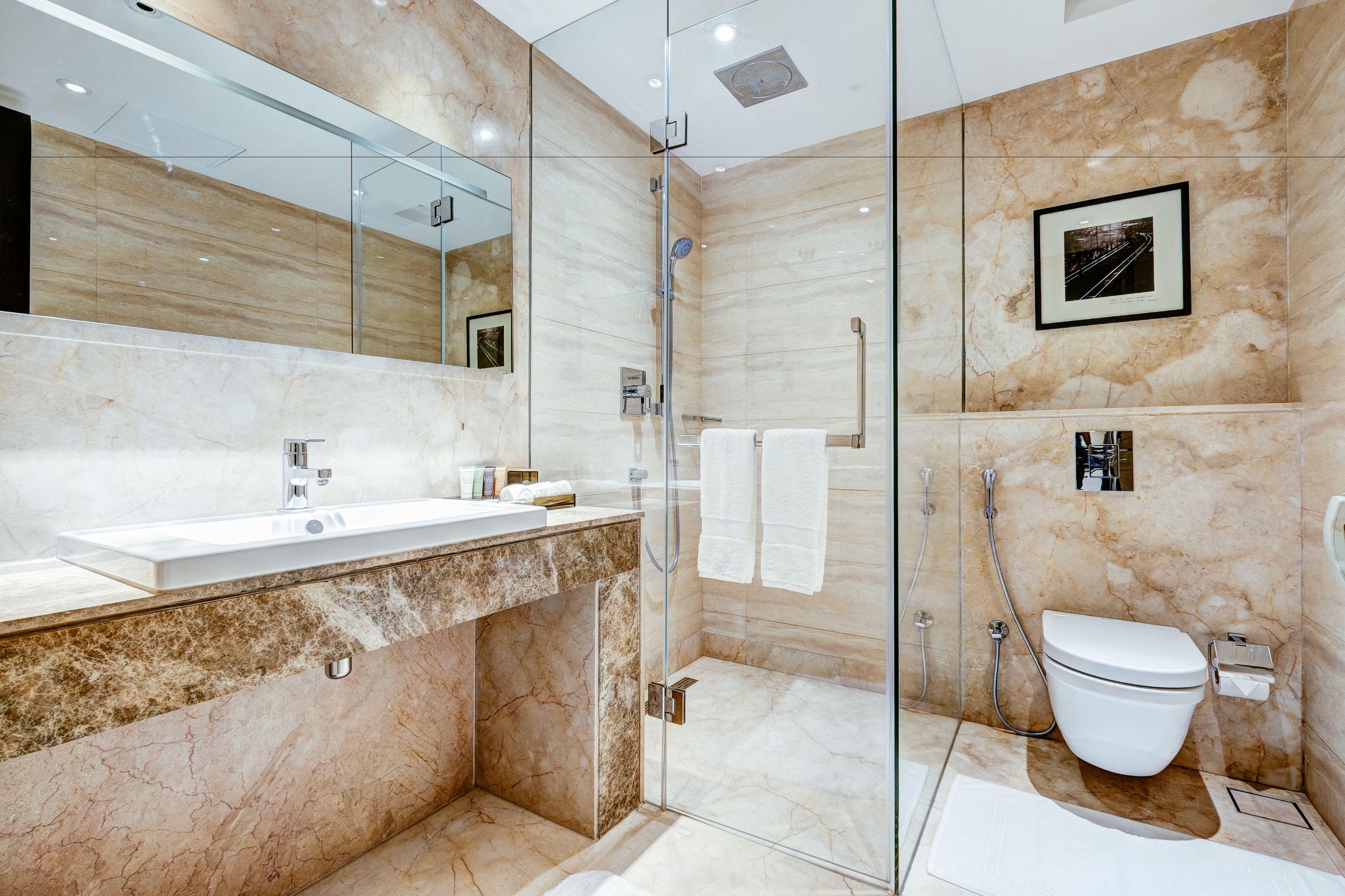 A modern bathroom with a glass-enclosed shower, a white sink, and a marble-tiled wall.