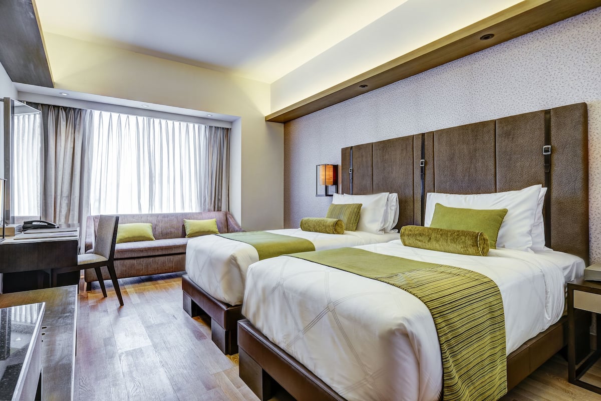 Ett hotellrum med två sängar, ett skrivbord, en stol och ett stort fönster med gardiner.