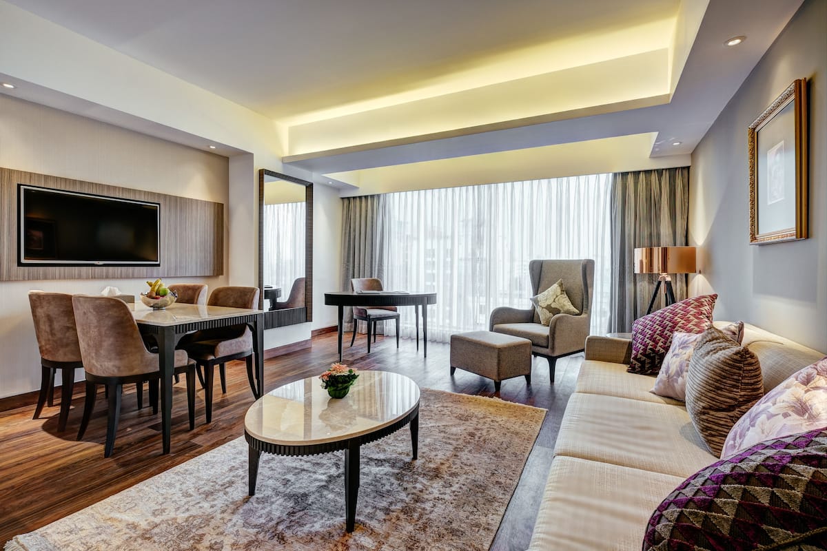 Ett modernt hotellrum med en matplats, en soffa, en TV och ett stort fönster med gardiner.