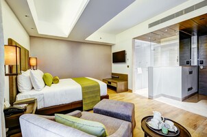 A hotel room with a bed, a desk, a chair, a small table with a tray of items, and a television.