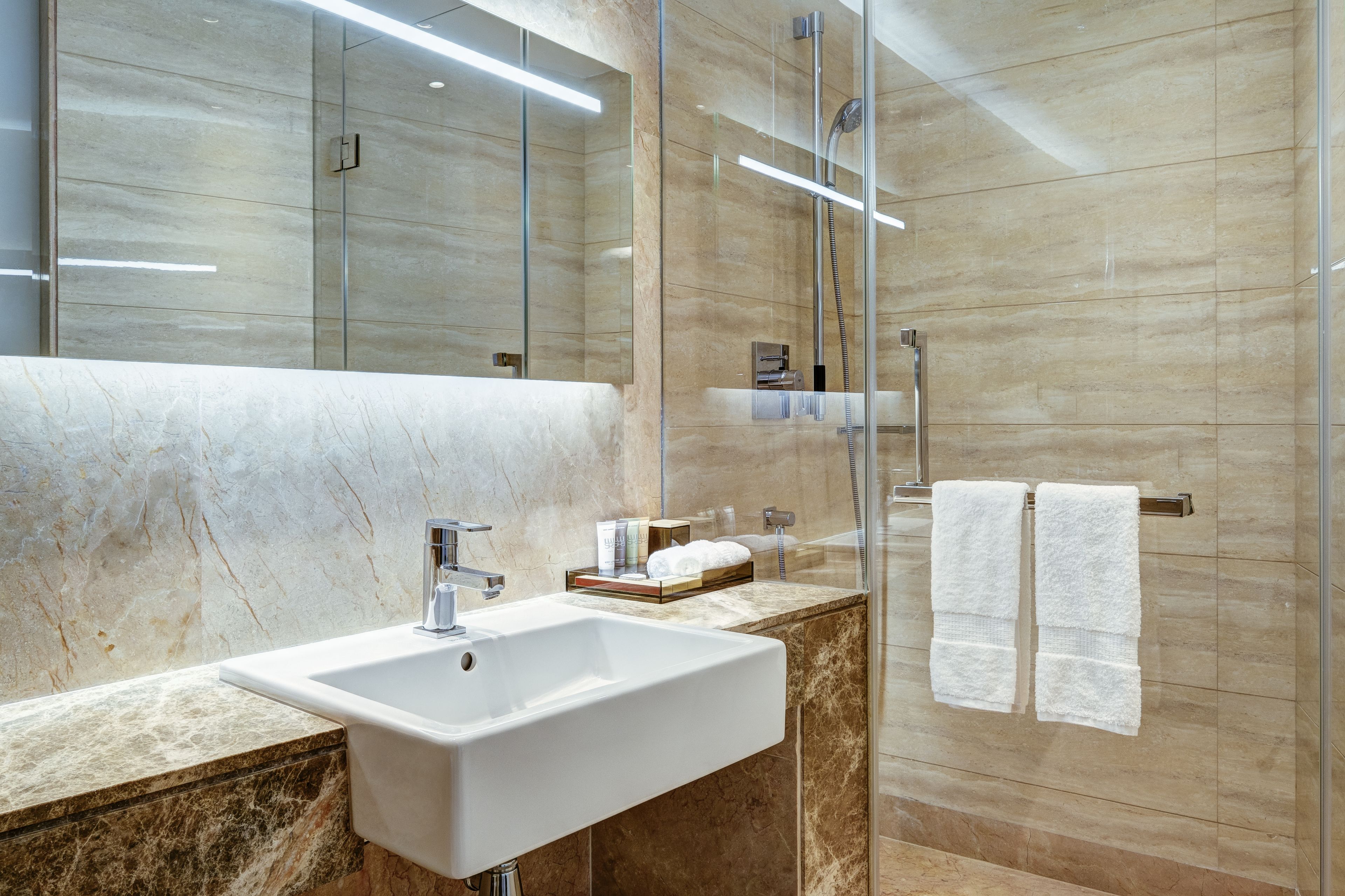 Un baño moderno con lavamanos de mármol, cabina de ducha de vidrio y un espejo grande.