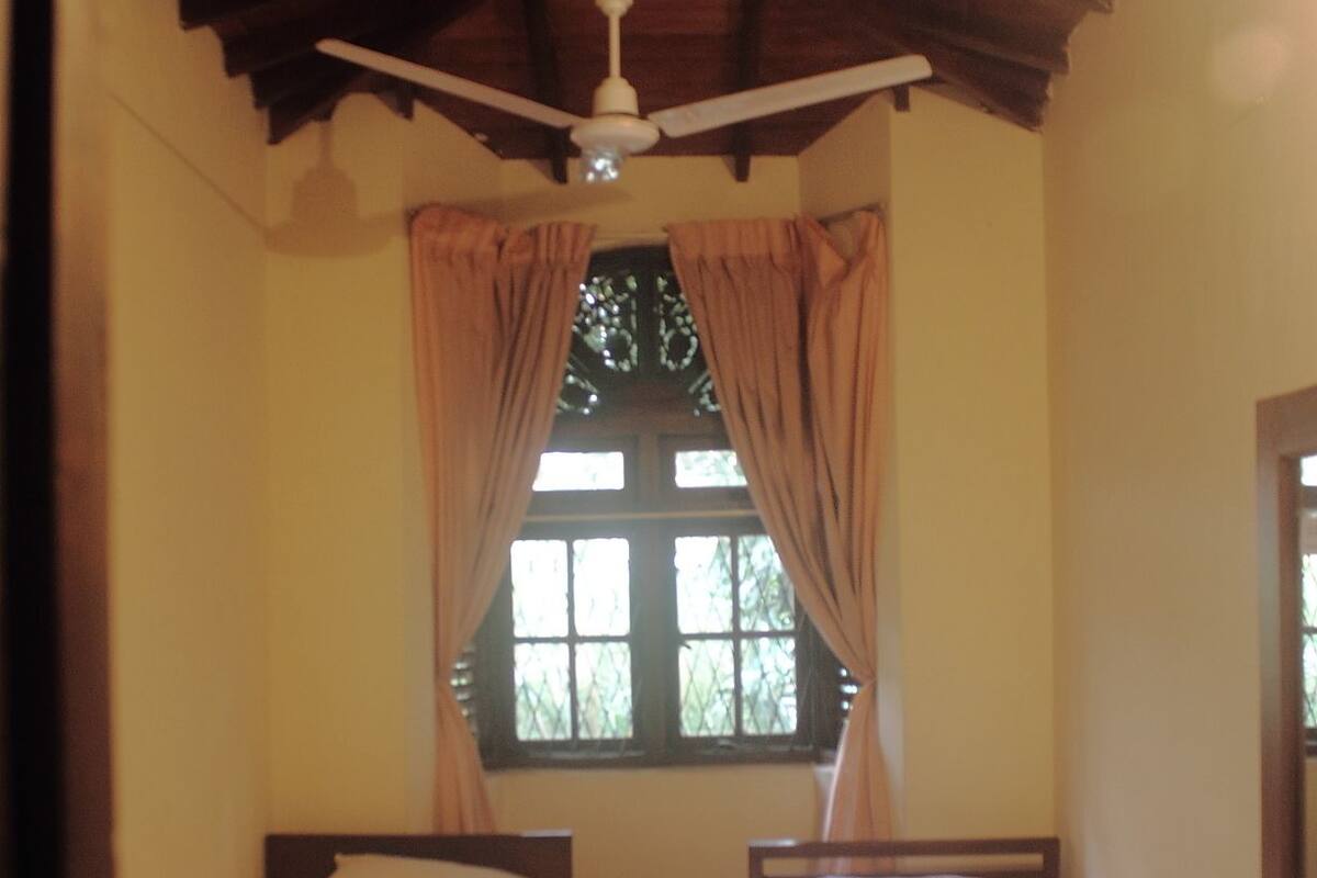 A room with two single beds, a ceiling fan, and a window with curtains.