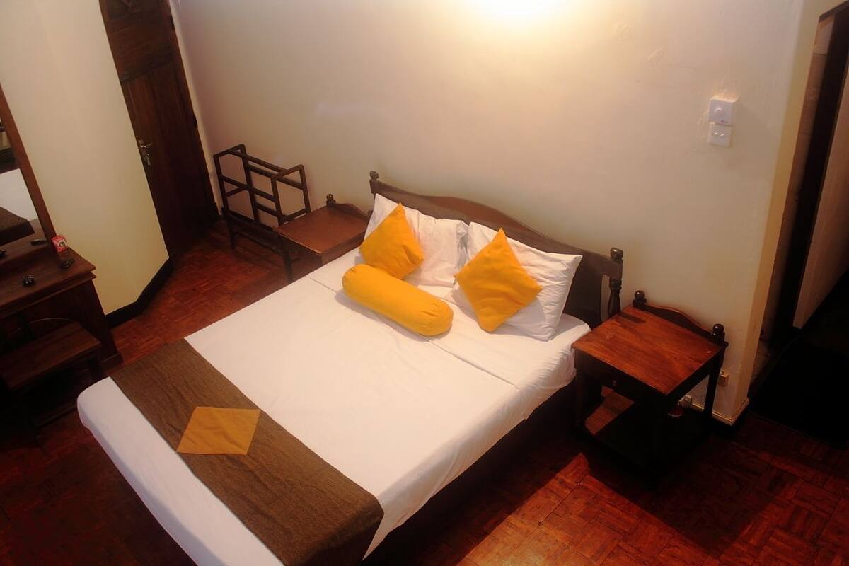 A neatly made bed with a white and brown bedspread, two yellow pillows, and a wooden nightstand with a lamp.