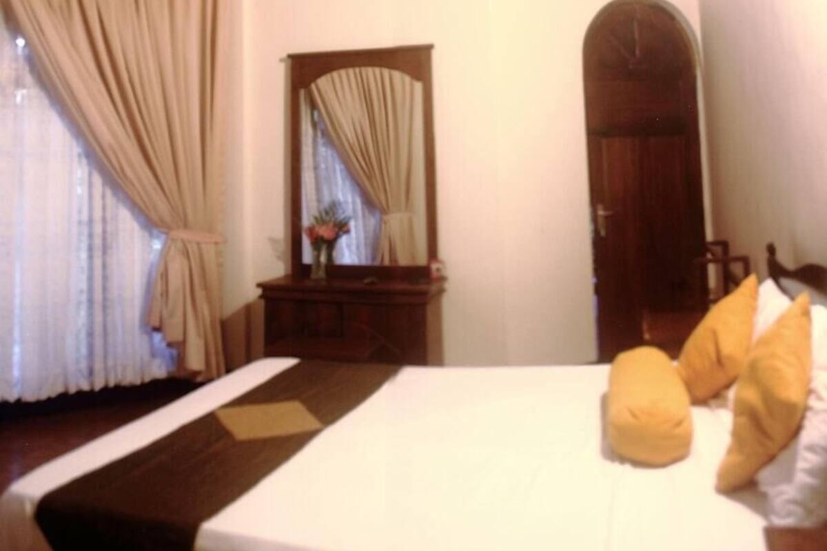 A bedroom with a bed, a wooden dresser, a mirror, and a door.