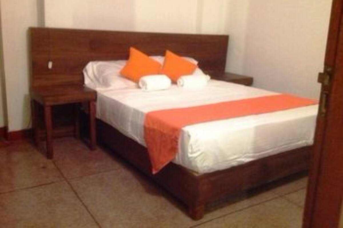 A single bed with a wooden headboard, white bedding, and orange pillows.