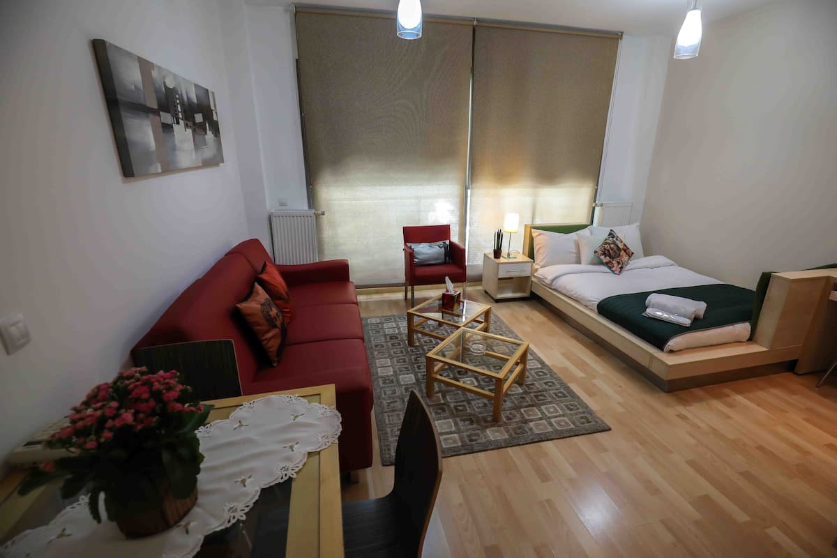 Una sala de estar moderna con un sofá rojo, una mesa de centro de madera y una cama con una manta verde.