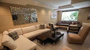 A modern living room with a beige sofa, two armchairs, a coffee table, and a decorative wall art piece. - Sky Suites (Beirut)