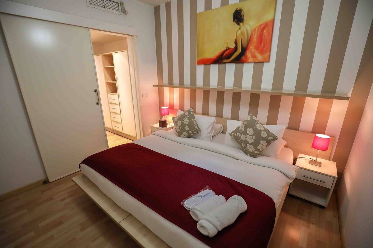 Habitación de hotel con cama, mesita de noche con lámpara, un cuadro en la pared y un armario.